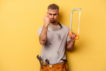 Young electrician caucasian man isolated on yellow background showing fist to camera, aggressive...