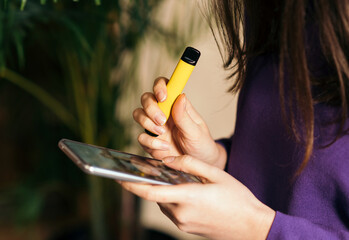 Yellow disposable electronic cigarette in a woman's hand. Modern online communication