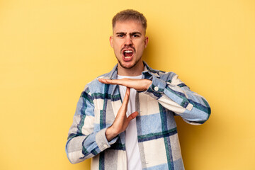 Young caucasian man isolated on yellow background showing a timeout gesture.