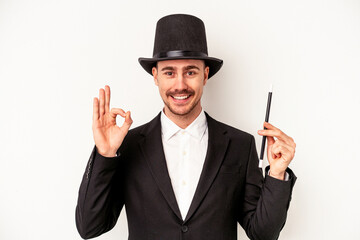 Young caucasian wizard man holding a wand isolated on white background cheerful and confident showing ok gesture.