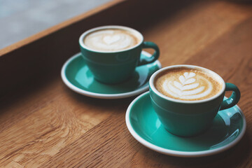 Two beautiful cups of cappuccino on the table. Decorated with perfect heart shape latte art. Coffee break, time in cafe, relax and enjoy the hot drink concept. Side view. Copy space for your text.