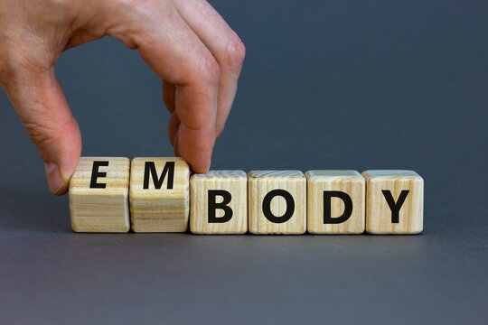 Body and embody symbol. Doctor turns wooden cubes and changes the concept word body to embody. Beautiful grey table, grey background, copy space. Medical, body and embody concept.