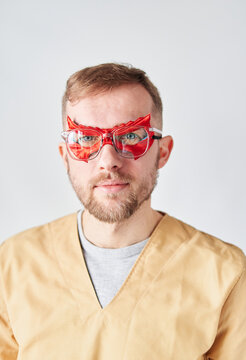 Close up portrait of a male superman doctor or nurse. Portrait of a handsome caucasian male doctor wearing red face superhero mask, eyeglasses and beige medical uniform. High quality vertical photo
