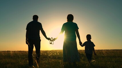 Fototapeta na wymiar The concept of building a family house. Real estate investment. The family holds a paper house in their hands, a child walks with parents at sunset. Dream of buying a house. Symbol of happiness.