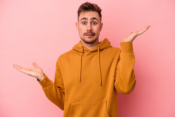 Young caucasian man isolated on pink background confused and doubtful shrugging shoulders to hold a copy space.
