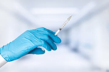 Hand wearing blue glove holding syringe. Laboratory background.