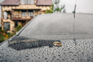 two gold wedding rings against a background of glossy black metal covered with raindrops