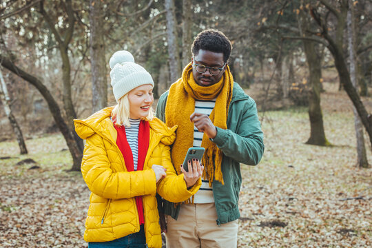A happy young couple in love with friends of travelers dressed in a casual style using a mobile phone in the woods of a nature park. They try to use navigation to find the desired location