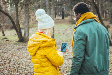 A happy young couple in love with friends of travelers dressed in a casual style using a mobile phone in the woods of a nature park. They try to use navigation to find the desired location
