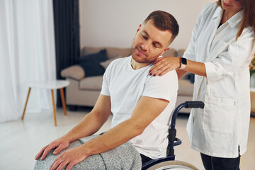 Fototapeta premium Woman is helping. Disabled man in wheelchair is at home