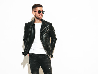 Portrait of handsome confident model. Sexy stylish man dressed in biker leather jacket and black jeans. Fashion hipster male isolated on white in studio. In sunglasses