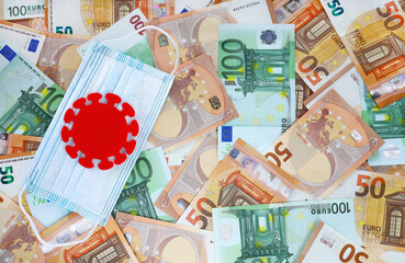 Red felt covid virus on blue medical mask on 50 and 100 euro banknotes background. Coronavirus pandemic in Europe. Financial crisis, bank, money, economy, business concept. Place for your text.