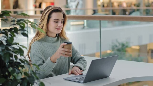 Caucasian business female freelancer student designer worker sitting at table in cafe office corporate space working with laptop typing message drinking coffee tea e-learning online shopping free wifi