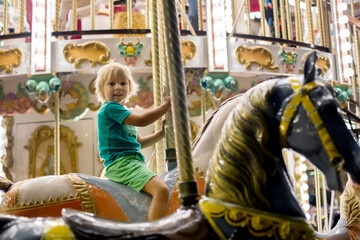 Sweet child, cute blond boy, riding on a merry-go-round, carousel attraction in Europe