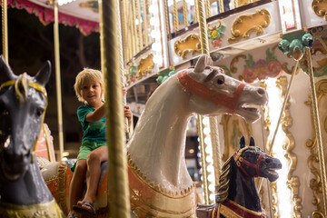 Sweet child, cute blond boy, riding on a merry-go-round, carousel attraction in Europe