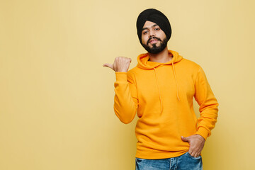 Bearded south asian man wearing turban pointing finger aside