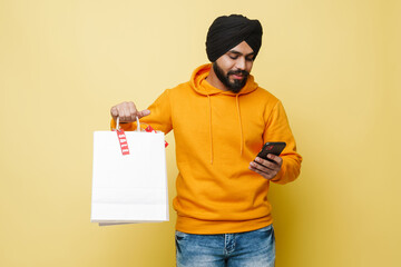 Fototapeta na wymiar Bearded south asian man using cellphone while posing with shopping bags