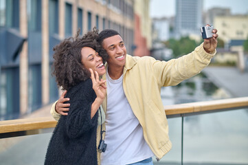 Man taking selfie with woman showing freedom gesture