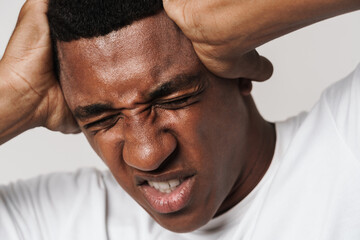 Young black man in t-shirt frowning while holding his head