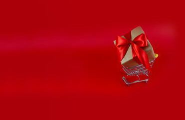 Gift with a red bow in a shopping cart on a red background. copy space. Festive background