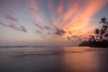 Fototapeta na wymiar golden sunset in sri lanka with traditional fishing stilts in the distance