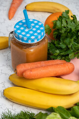 Fruit and vegetable smoothie in jar with straw. There are carrots, bananas, and greens nearby. Close-up from above. Selective focus.