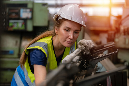 woman engineer wear hardhat working at machine in factory. female technician control metalwork lathe industrial.