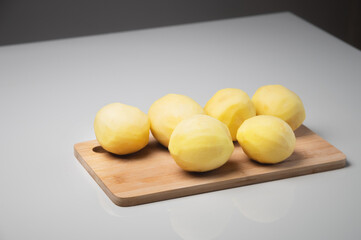 Peeled fresh potatoes on a wooden cutting board on a white table.
