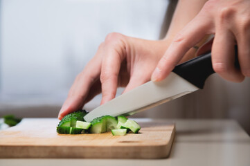 Close-up of female hands cutting cucumbers for a vegan salad. Home cooking healthy and wholesome food