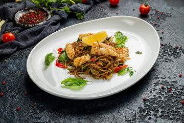 Fried soba noodles with fried squid and vegetables on dark stone table, Chinese cuisine