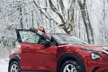 Walking out off car. Beautiful young woman is outdoors near her red automobile at winter time