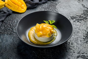 panna cotta with mango and mint on black bowl on dark stone table, Chinese cuisine