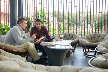 Business people sitting in office building lounge area and discussing report on tablet computer