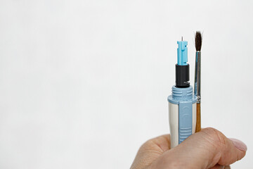 Female hand on a white background holds a lancet and an artistic brush