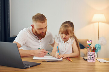 Using laptop. Father with his little daughter is at home together