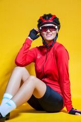 Cycling Ideas. Closeup Portrait of Confident Positive Female Road Cyclist in Professional Outfit Sitting On Floor Against Yellow Background.
