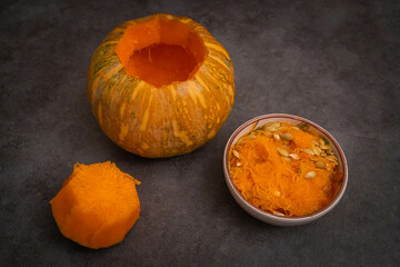 Small ripe pumpkin with carved lid and seeds in bowl on dark background