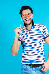 Funny Positive Smiling Caucasian Handsome Guy Posing With Artistic Paper Red Glasses in Casual Clothing Against Seamless Blue Background.