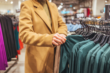 Naklejka premium Female customer chooses clothes in a store, a blonde looks at a T-shirt in a boutique on a hanger, a woman buys on sale. The concept of shopping