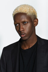 portrait of blonde african american man in black blazer isolated on grey.