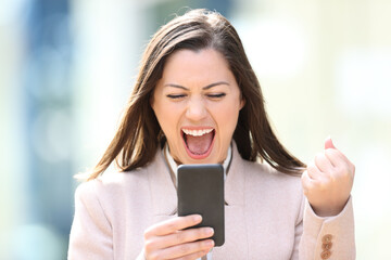 Excited businesswoman checking smart phone outdoors