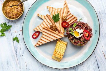 French cuisine, beef steak tartare with raw quail egg yolk, capers, pickled cucumber with bread toasts served on plate. Food recipe background. Close up