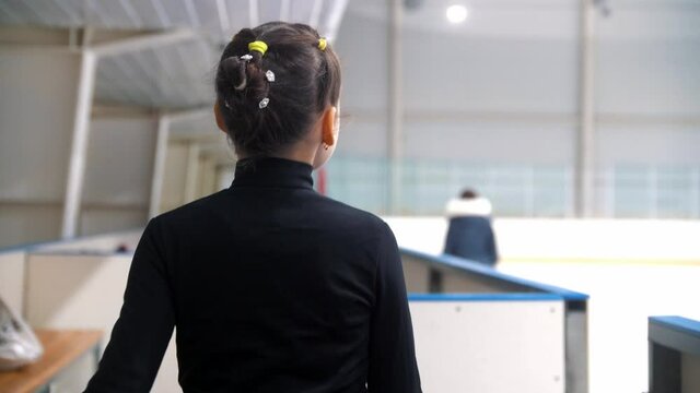 A girl figure skater walks to the gates of the public ice rink and about to go on the ice