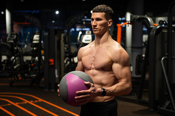 Muscular guy with fit torso holding medicine ball in gym, workout