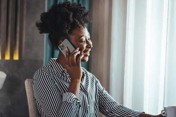 Fototapeta na wymiar Corporate communication. A black business woman talking on a mobile phone working on a laptop in a modern office. Solves problems over the phone. free space