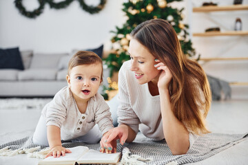 Sitting on the ground. Mother with her little daughter is indoors at home together