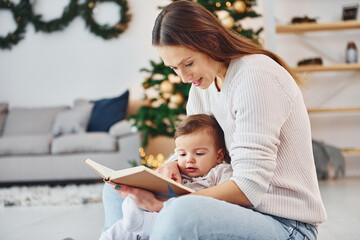 Sitting on the ground. Mother with her little daughter is indoors at home together