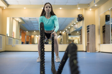 A young woman trains with a battle rope in a fitness room for functional training