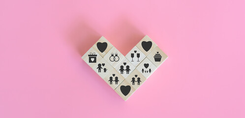Love is and Valentine's Day concept. The cube wooden blocks are arranged in a heart shape with icons such as family, pet lover, LGBTQ, ring, champagne, and gift on pink background.