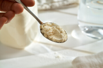 Hand holding a spoon with whey protein powder above white background